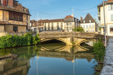 Güneşli bir sabahta Fransa 'nın Salies de Bear kasabasında sakin bir nehirde yansıyan eski taş köprünün manzarası.
