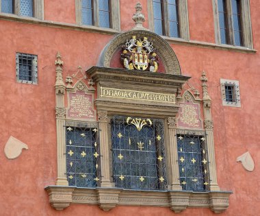 Mimari detay, Prag 'daki canlı, tarihi bir binada armalı, latin yazıtlı ve dekoratif demiri olan süslü bir pencere sergiliyor.