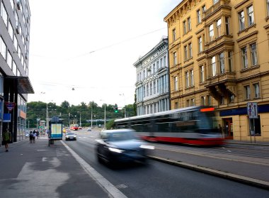 Prag 'da bir caddede hızlı geçen modern tramvay. Bulanık araba, otobüs durağı ve renkli binalar.