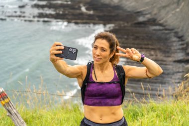 Kadın yürüyüşçü zafer işaretiyle selfie çekiyor Zumaia, Bask ülkesindeki Sakoneta plajında yürüyüş yaparken, İspanya