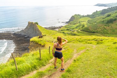 Sakoneta plajının ve zumaia, gipuzkoa 'daki sahil sineğinin manzarasının tadını çıkaran bir bayan sporcu.