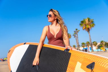 Sörfçü, sörf tahtasıyla kumlu sahil boyunca okyanus dalgaları ve tropikal titreşimlerle dolu güneşli bir yaz gününün tadını çıkarıyor.