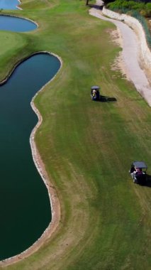 Gür yeşil bir pistte yol alan golf arabası, resimli bir su engelinin etrafında ustaca manevra yapıyor.