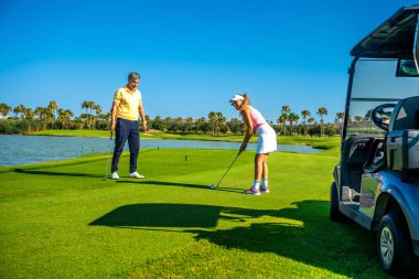 Güneşli bir günde golf oynayan çift, sporun ve parkuru çevreleyen büyüleyici manzaranın tadını çıkarıyor.