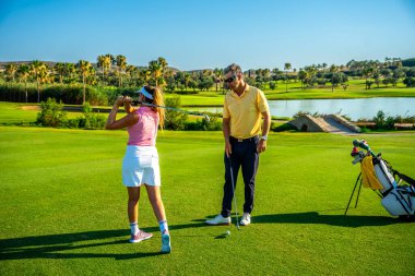 Golfçü güzel bir golf sahasında koçla vuruş talimi yapıyor, tekniğini geliştirmeye çalışıyor.