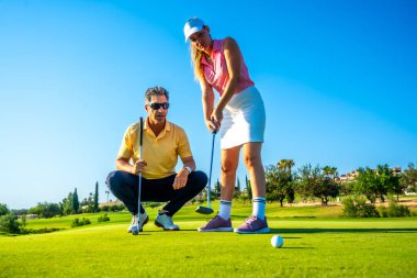 Kadın golfçü sıcak güneşin altında eğitmeninden tavsiye alıyor, golf sahasında teknik ve beceri geliştirmeye odaklanıyor.