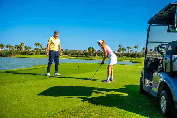 Güneşli bir günde golf oynayan çift, sporun ve parkuru çevreleyen büyüleyici manzaranın tadını çıkarıyor.