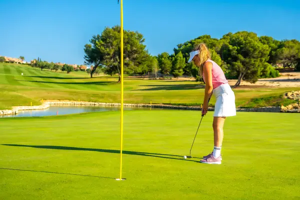 Kadın golfçü, güneşli bir günde golf sahasında topu deliğe sokmaya konsantre oluyor.