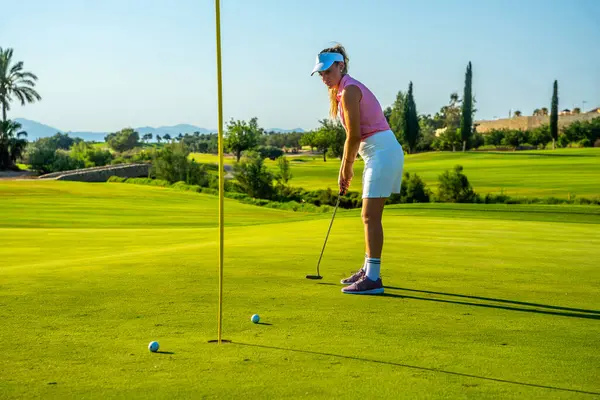 Golf sahasında güneşli bir günde topu deliğe sokmaya odaklanan profesyonel bir golfçü.