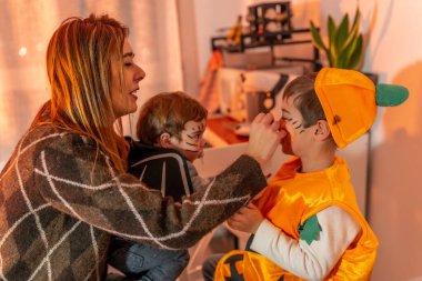 Annem evlerinde yarasa ve balkabağı gibi giyinmiş iki oğluna cadılar bayramı makyajı yapıyor.