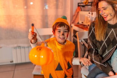 Balkabağı kostümü giymiş mutlu bir çocuk elinde plastik bir fenerle cadılar bayramını kutluyor.