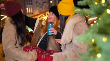 Noel hediyelerini değiş tokuş eden ve Noel pazarında sıcak içeceklerin keyfini çıkaran üç neşeli kadın.