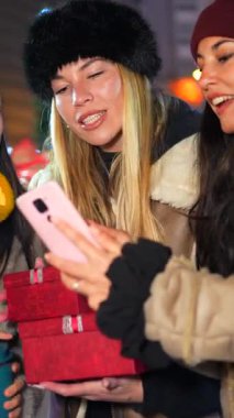 Şenlikli bir gece pazarında Noel hediyelerini paylaşan iki neşeli kadın, bir akıllı telefonla anı yakalıyorlar.