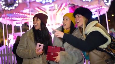 Üç mutlu bayan arkadaş yılbaşı pazarında eğleniyor, hediyeler alıyor ve festival atmosferinin tadını çıkarıyorlar.