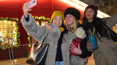 Üç kız arkadaş yılbaşı gecesi fotoğraf çekiyor ve akıllı telefondan fotoğraf izliyorlar.