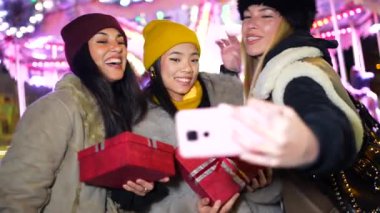 Üç neşeli bayan arkadaş selfie çekiyor ve gece bir Noel pazarında eğleniyorlar.