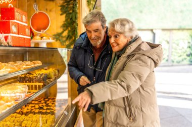 Mutlu son sınıf çifti, hareketli bir Noel pazarında lezzetli pastaları göstererek ve seçerek neşeli atmosferin tadını çıkarıyor.