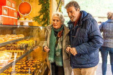 Bayram sezonunda açık hava pazarında lezzetli noel pastaları ve pastalara bakan yaşlı bir çift.
