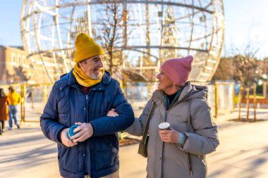 Kış boyunca şehirde kol kola yürüyen gülümseyen yaşlı çift sıcak bir içecek ve Noel süslemelerinin tadını çıkarıyorlar.