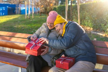 Yaşlı çift, güneşli bir kış gününde şehir parkında bir bankta otururken Noel hediyelerini değiş tokuş ediyorlar.