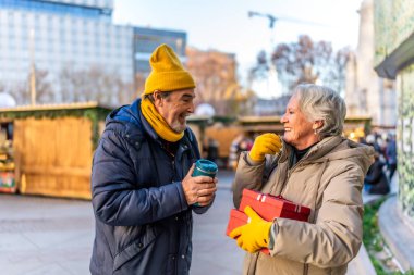 Yaşlı çift, Noel hediyelerini değiş tokuş ediyor ve kış tatillerinde geleneksel bir Noel pazarında sıcak bir içecek içiyor.