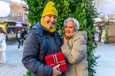Gülümseyen son sınıf çifti Noel hediyesi taşıyor, kış tatillerinde şehirdeki Noel pazarının keyfini çıkarıyorlar.
