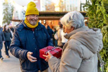 Mutlu kıdemli bir adam, şehirde hareketli bir tatil pazarının neşeli atmosferinin tadını çıkarırken karısına bir Noel hediyesi sunuyor.