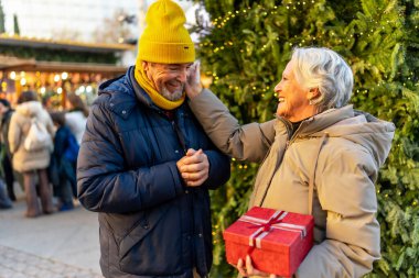 Geleneksel Noel pazarında Noel hediyelerini değiş tokuş eden, neşeli atmosferin tadını çıkaran ve değerli anları paylaşan yaşlı çiftler.