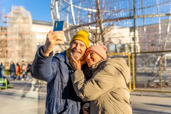 Kış şehir merkezinde Noel 'de akıllı telefonuyla selfie çeken gülümseyen yaşlı çift.
