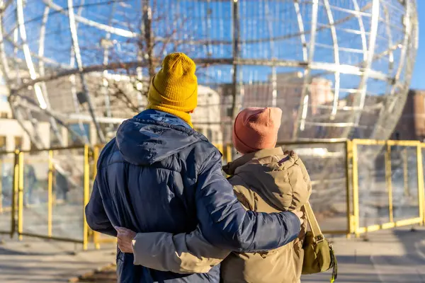 Yaşlı çift, bir kış şehri manzarasında büyük noel balosu süslemelerine hayran kalarak kucaklaşıyor.