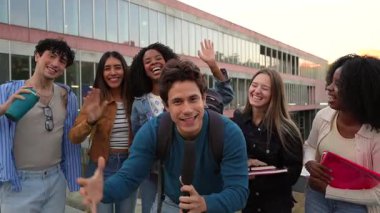 Enerjik öğrenci gazeteci mikrofonla bildirirken, çeşitli sınıf arkadaşları kameraya el sallıyor ve gülümsüyor. Üniversite kampüsünde birlikte kutlama yapıyorlar.