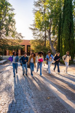 Ders kitapları ve sırt çantalarını kaldırım taşlı bir yolda aceleyle taşıyan çeşitli üniversite öğrencileri, kampüste sabah güneşinin altında neşe ve enerji ifade ediyorlar.
