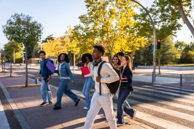Üniversite öğrencilerinden oluşan çok ırklı bir grup kampüs yaya geçidinde yürüyorlar. Sırt çantaları ve kitaplar taşırken gülümsüyorlar ve sohbet ediyorlar. Arkadaşlığı, öğrenmeyi ve gençlik enerjisini simgeliyorlar.