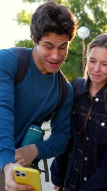 Çeşitli mutlu üniversite öğrencileri, okuldan sonra kampüste birlikte yürüyüp, gülüyor ve akıllı bir telefon kullanırken, öğleden sonra güneşinin altında parlak bir mercek oluşturuyorlar.