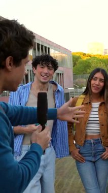 Elinde mikrofonla gülümseyen ve sohbet eden üç genç üniversite öğrencisi üniversite kampüsünde yan yana dururken fikirlerini ve deneyimlerini paylaşıyorlar.