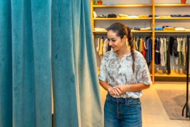 Düşünceli bir ifadeyle, mağazanın soyunma odasında kıyafet deneyen bir kadın.