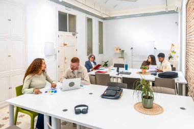 Fikirleri tartışan, belgeleri analiz eden ve modern ofis alanındaki ortak bir toplantıda dizüstü bilgisayarlar üzerinde çalışan bir grup iş adamı.