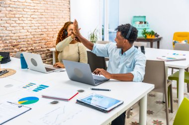 Laptoplarda çalışan çeşitli iş arkadaşları, modern bir ofis alanında ortak bir başarıyı veya başarılı bir projeyi kutlamak için beşlik çakıyorlar.