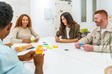 Modern bir ofis atölyesinde işbirliği yapan çok kültürlü meslektaşlar, beyaz bir masa üzerinde renkli yapışkan notlar düzenlerken, fikirler üzerinde beyin fırtınası yaparken, projeler planlarken ve yenilikleri teşvik ederken,