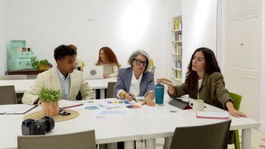 Modern bir ofiste işbirliği yapan, grafikleri ve grafikleri analiz eden, iş stratejilerini tartışan ve önemli bir proje planlama toplantısında fikir alışverişinde bulunan çeşitli meslektaşlar.