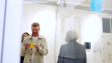 Modern bir ofiste başarılı bir iş stratejisi geliştirmek için beyin fırtınası sırasında cam bir tahtaya renkli yapışkan notlar yerleştirerek bir proje üzerinde çalışan yaratıcı çok ırklı ekip.