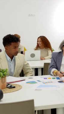 Modern ve parlak ofis konferans odasında yapılan verimli bir şirket toplantısında proje istatistiklerini ve grafiklerini tartışan çok nesilli ve çok ırklı iş adamları.