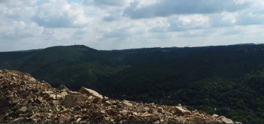 Yoğun orman ve bulutlu gökyüzü ile kaplı bir tepe manzarası