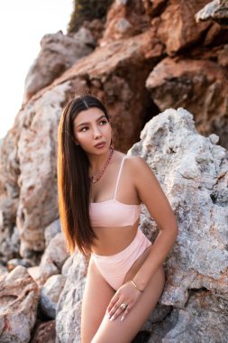 Beautiful model in swimsuits on a rock near the sea.