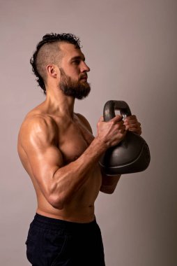 Genç kaslı bir adam arka planda bir kettlebell ile poz veriyor. Spor yaşam tarzı..
