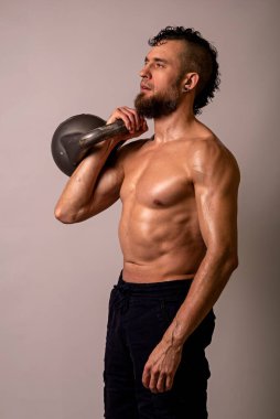 Genç kaslı bir adam arka planda bir kettlebell ile poz veriyor. Spor yaşam tarzı..