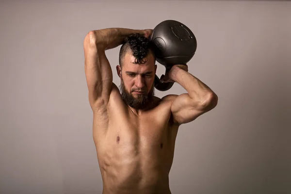 年轻的肌肉男摆设与轻盈背景的水壶铃铛 体育生活方式 — 图库照片