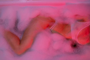 Seksi genç kadın köpük banyosu yapıyor. Erotik fotoğraf iç çamaşırlı, neon ışıklı..