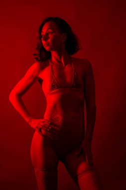 Kırmızı ışık altında iç çamaşırlı bir kadının portresi. Formda fiziğini ve ciddi ifadesini sergiliyor..