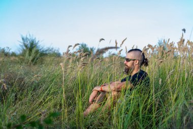 Gün batımında tarlada sakallı ve mohawk saçlı genç bir adam. Doğa.